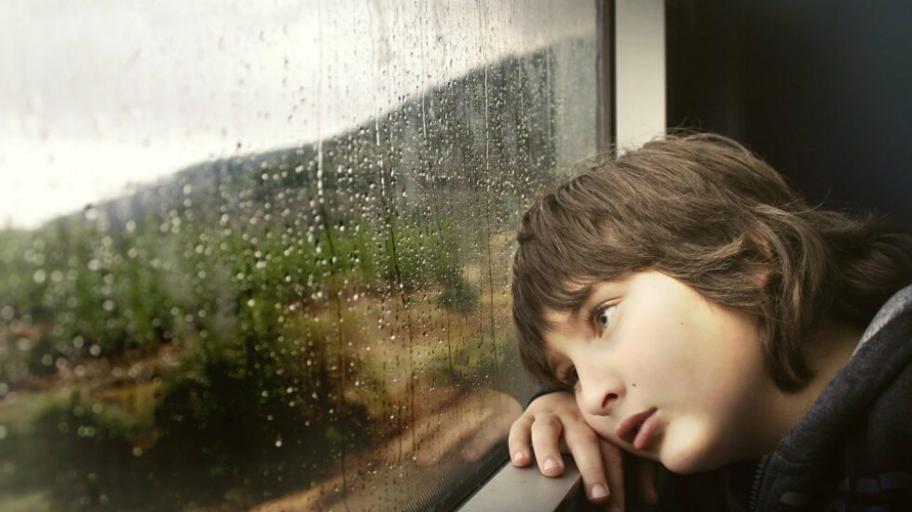 Kind guckt aus dem Fenster in den Regen Kind guckt aus dem Fenster in den Regen